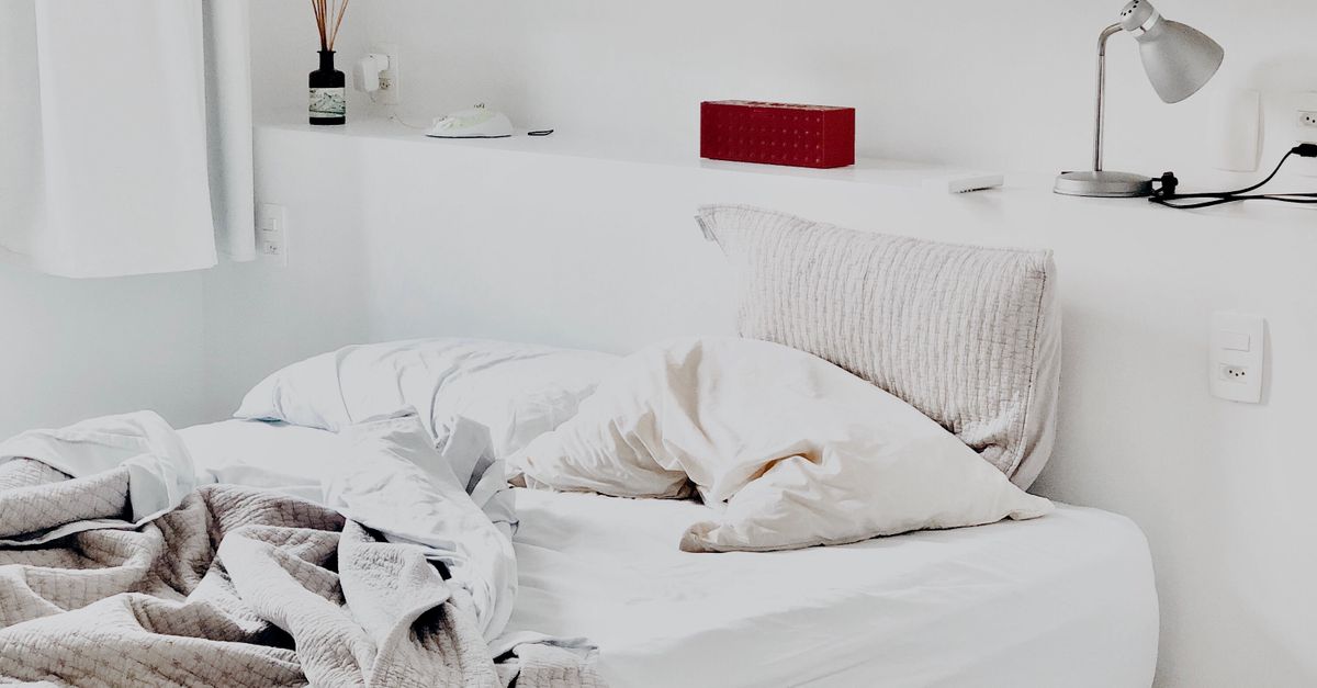 Onopgemaakt wit bed met meerdere kussens