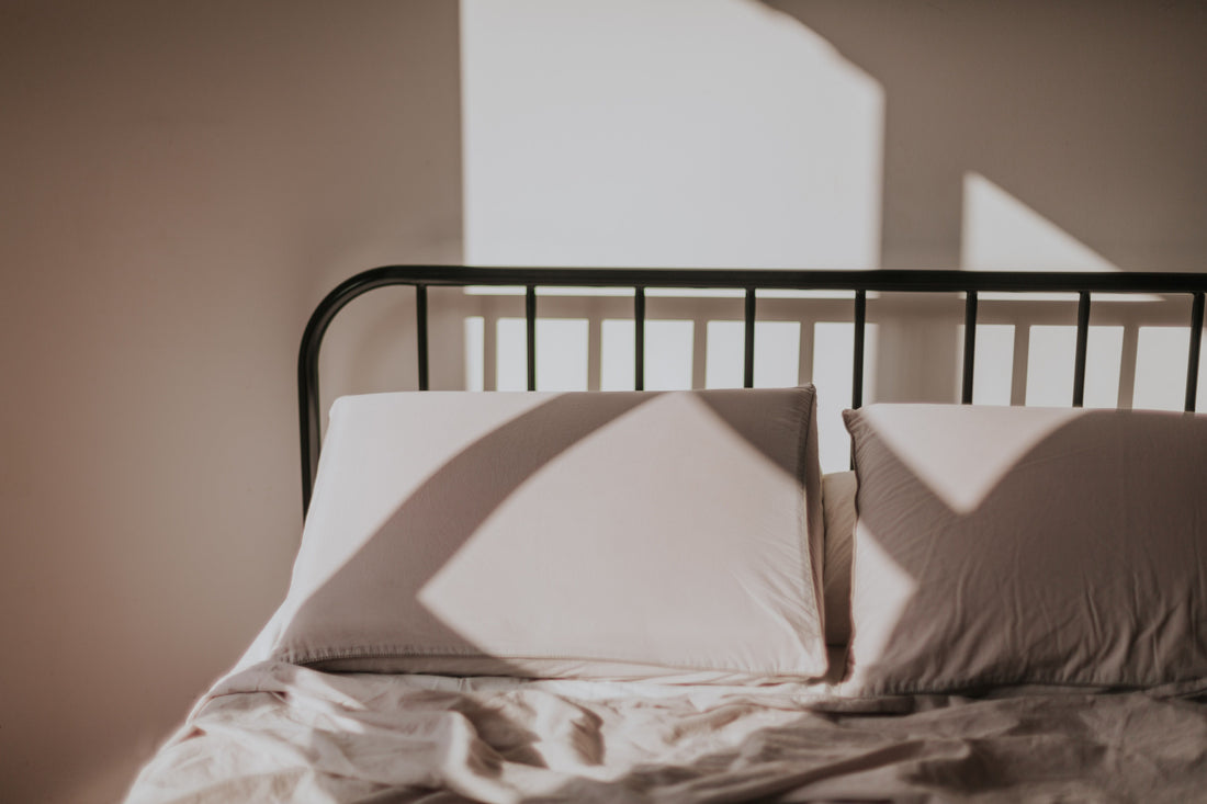 Opgemaakt bed met twee lichte kussens tegen een zwart spijlenhoofdbord in zonlicht