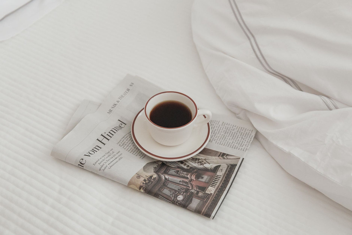 Kop zwarte koffie op een krant op wit beddengoed