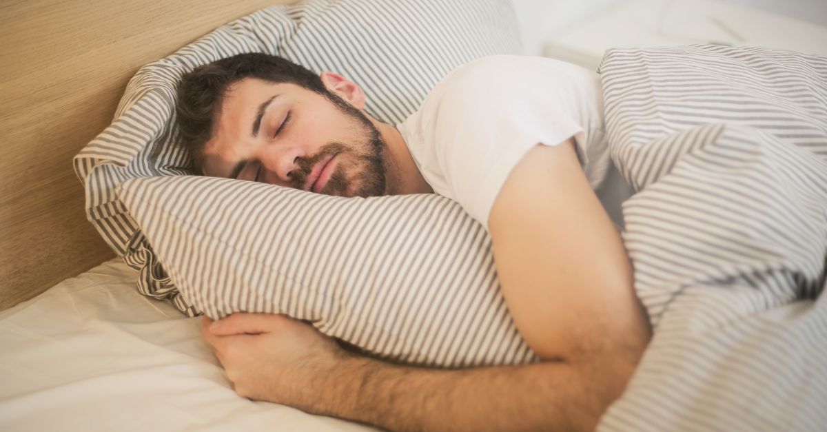 Man slaapt op zijn zij met zijn arm om een gestreept kussen geslagen