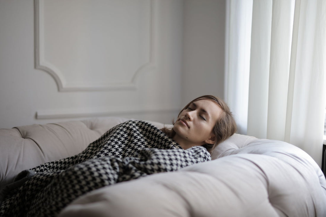 Vrouw doet een dutje op de bank onder een deken