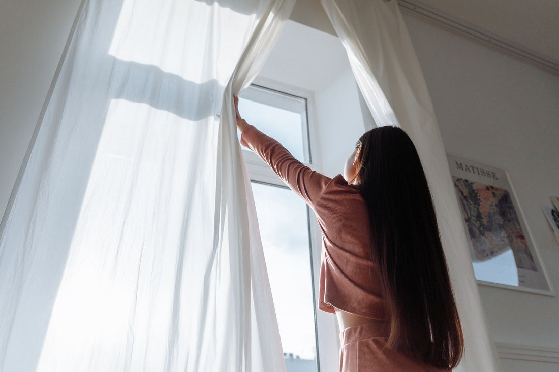 Vrouw opent de gordijnen voor een zonnig raam