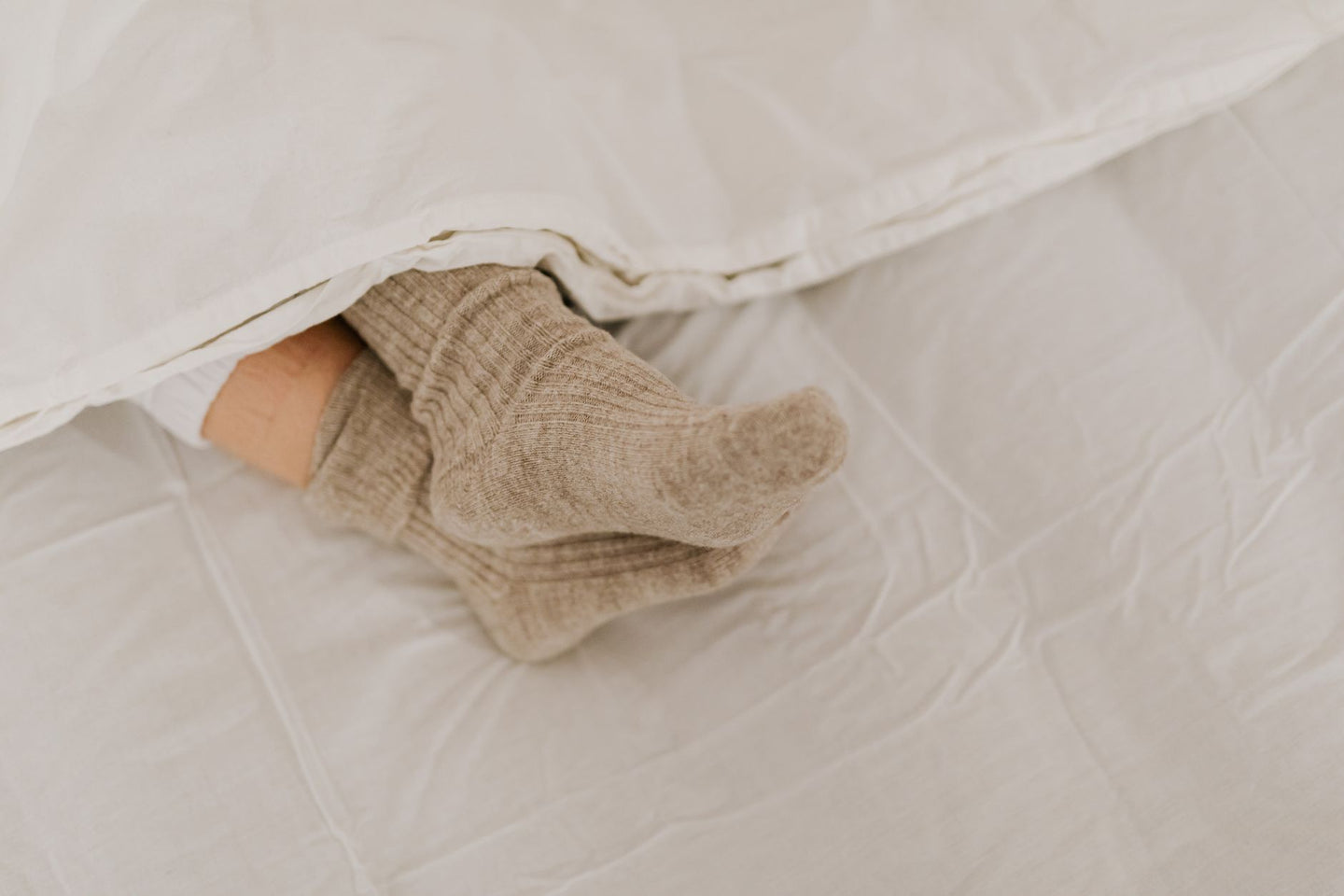 Voeten in wollen sokken steken onder het dekbed uit