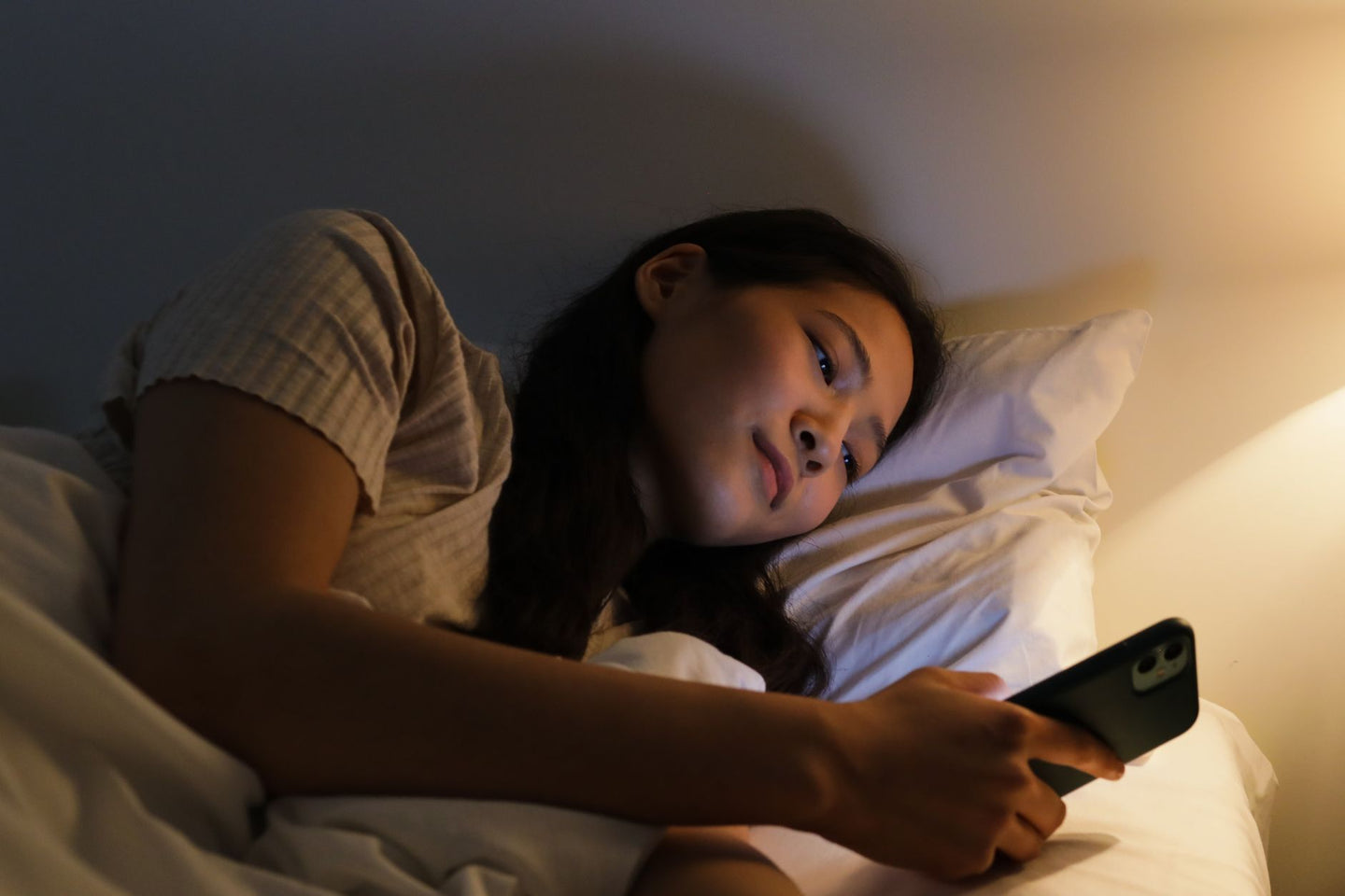 Vrouw ligt op haar zij in bed en kijkt naar haar telefoon