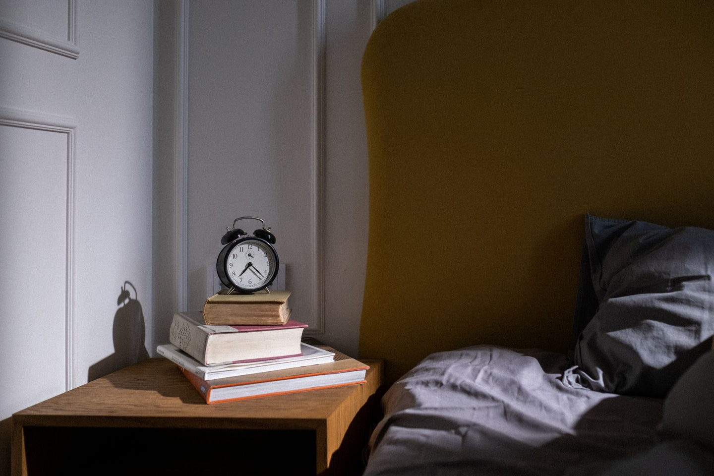 Klassieke wekker op een stapel boeken naast een bed