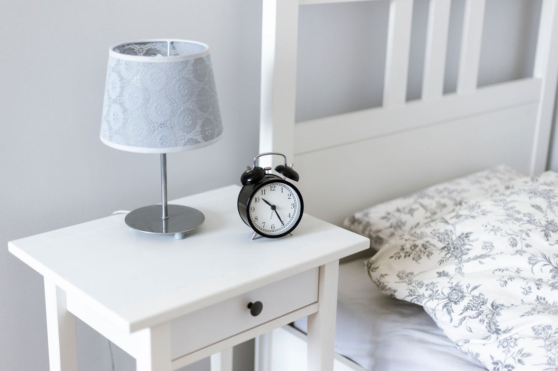 Analoge wekker en lamp op een wit nachtkastje naast het bed