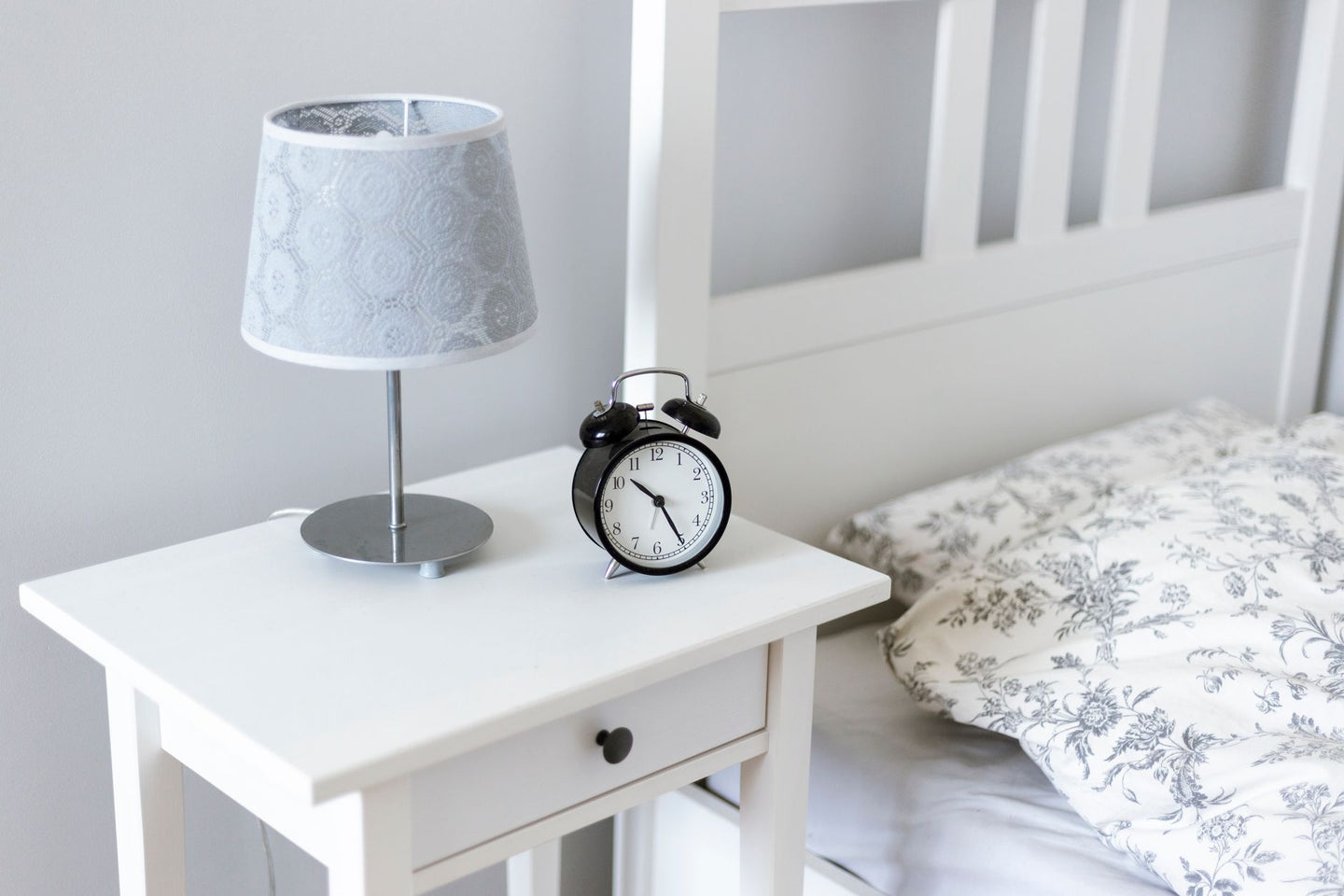 Analoge wekker en lamp op een wit nachtkastje naast het bed