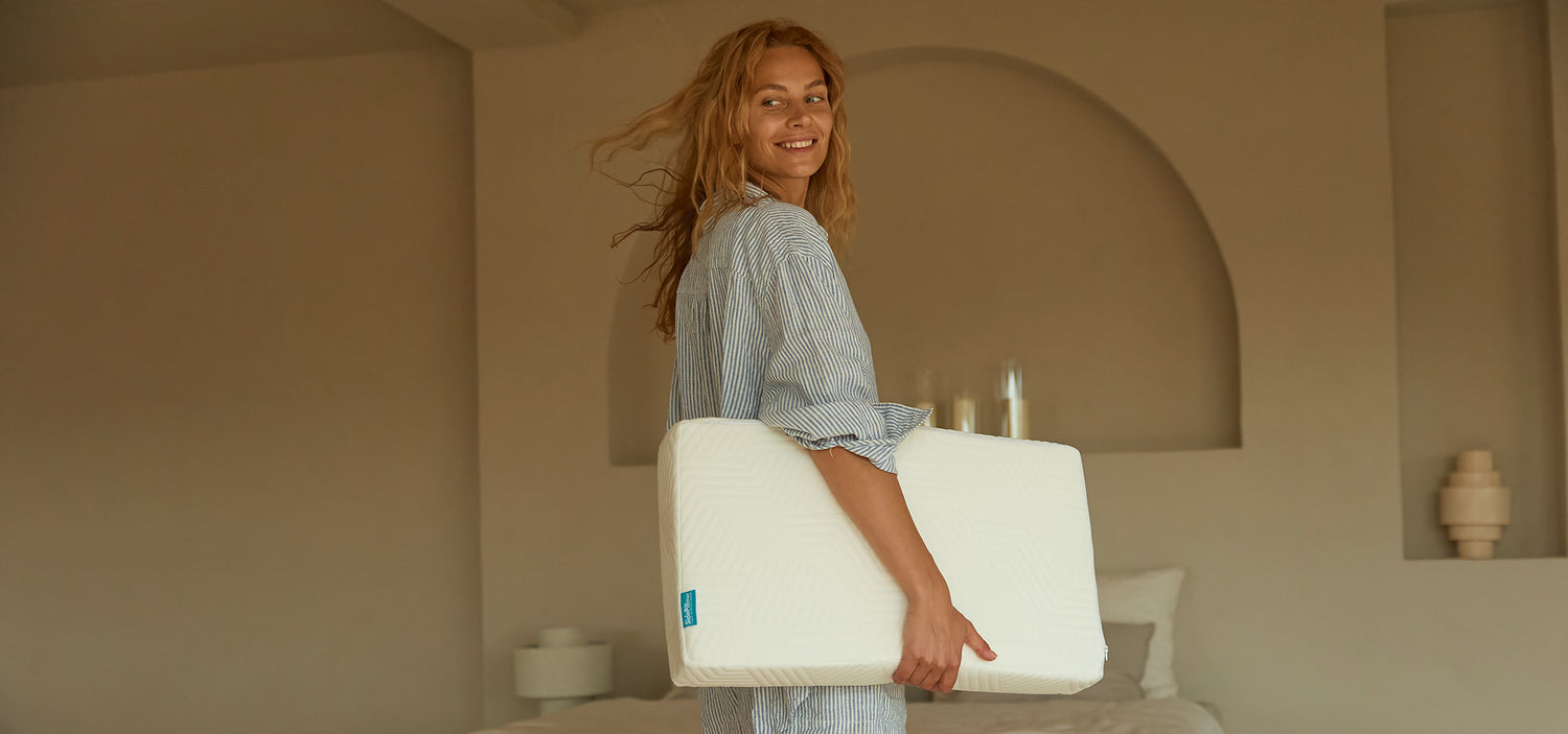 hero afbeelding vrouw met sidepillow kussen in handen vrolijk kijkend met een slaapkamer op de achtergrond